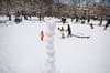 Children and their families play in Washington Square Park in front of a tower of snowballs