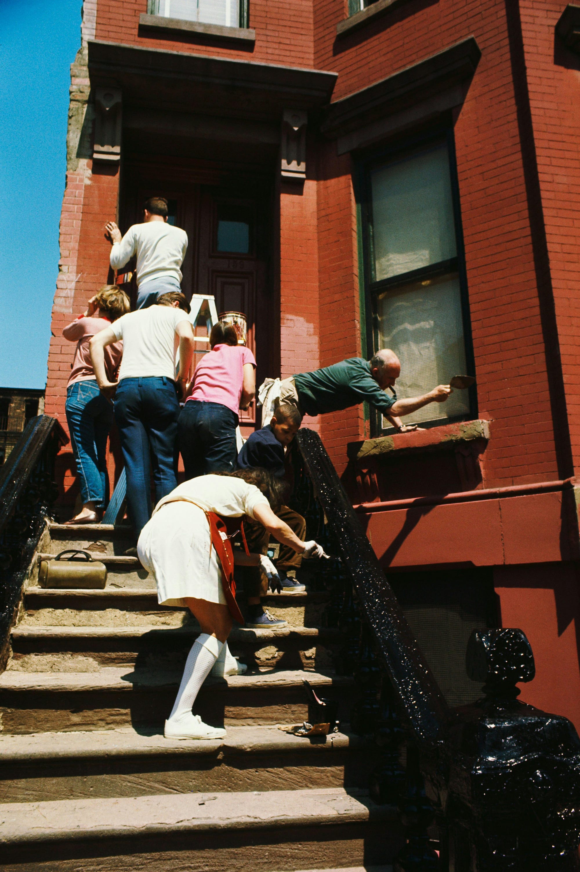 People paint the sides of a brownstone building